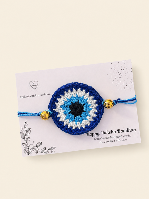 Handmade blue nazar crochet rakhi with gold-tone bead accents on a Raksha Bandhan card