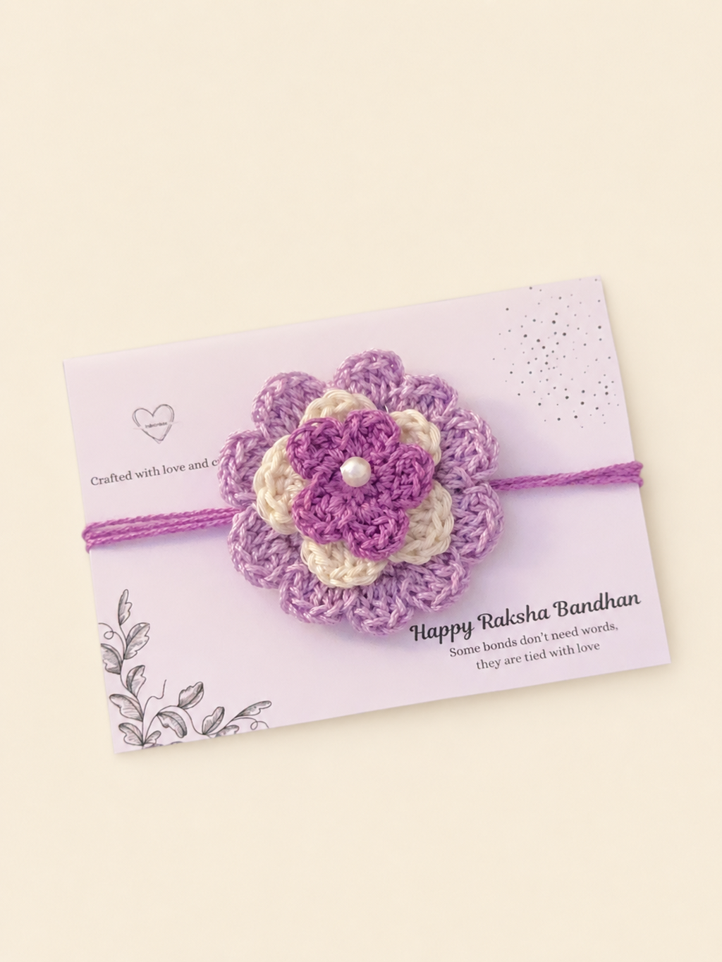 Handmade layered lavender and ivory floral crochet rakhi with purple ties on a Raksha Bandhan presentation card