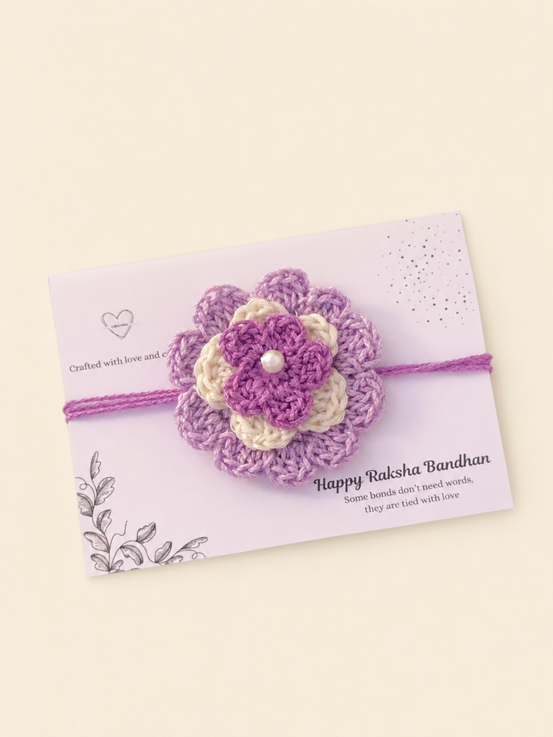 Handmade layered lavender and ivory floral crochet rakhi with purple ties on a Raksha Bandhan presentation card