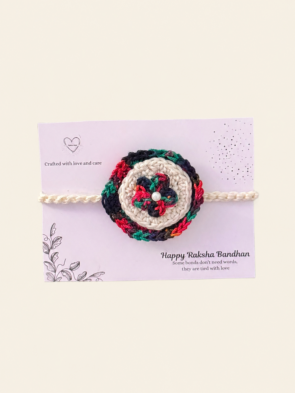 Handmade multicolour floral crochet rakhi with an ivory centre and cream ties on a Raksha Bandhan presentation card