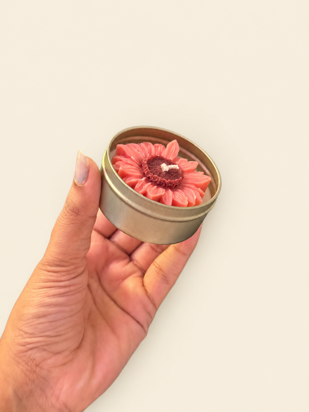 Hand-held view of the pink flower-shaped candle in its reusable metal tin