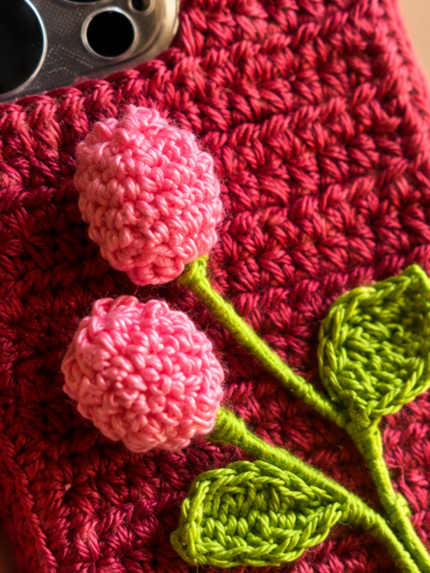 Close-up of pink crochet flower buds and green leaves on a deep pink phone cover