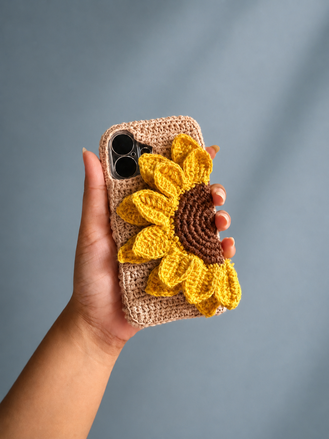 Handmade crochet sunflower phone cover held against a muted blue background