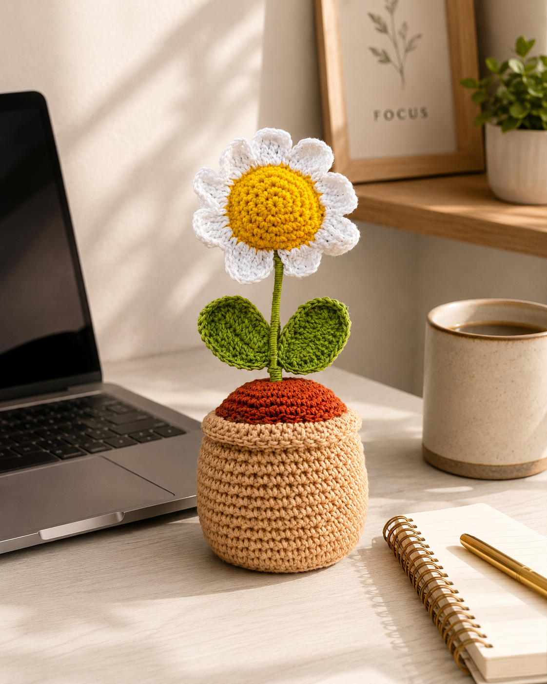 Handmade crochet daisy flower pot on a desk beside a laptop and coffee mug