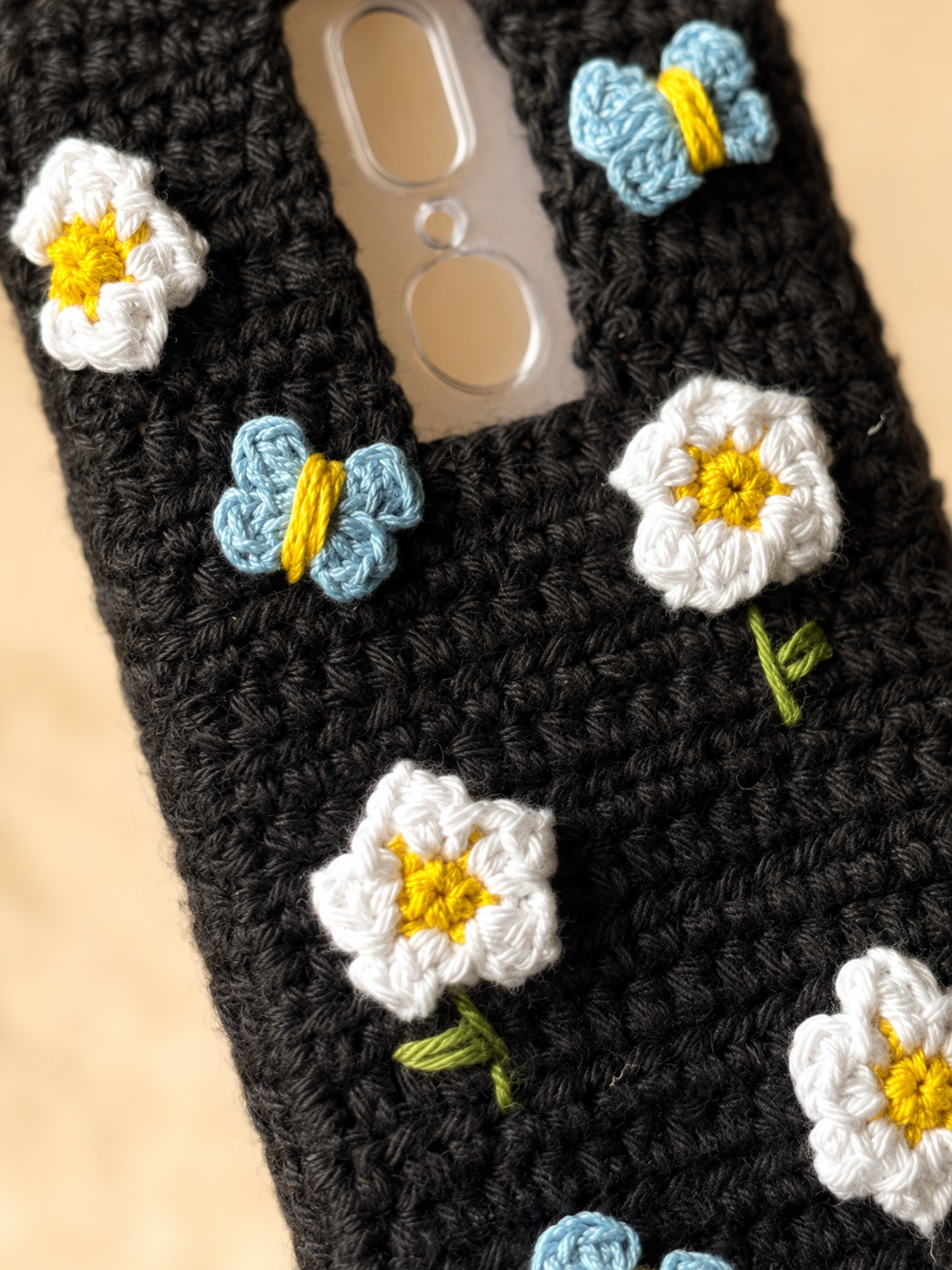 Close-up of white crochet flowers and blue butterflies on a black crochet phone cover