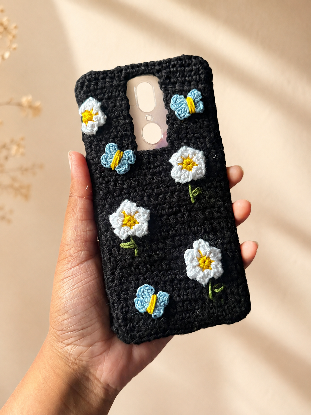 Handmade black crochet phone cover with white flowers and blue butterfly details