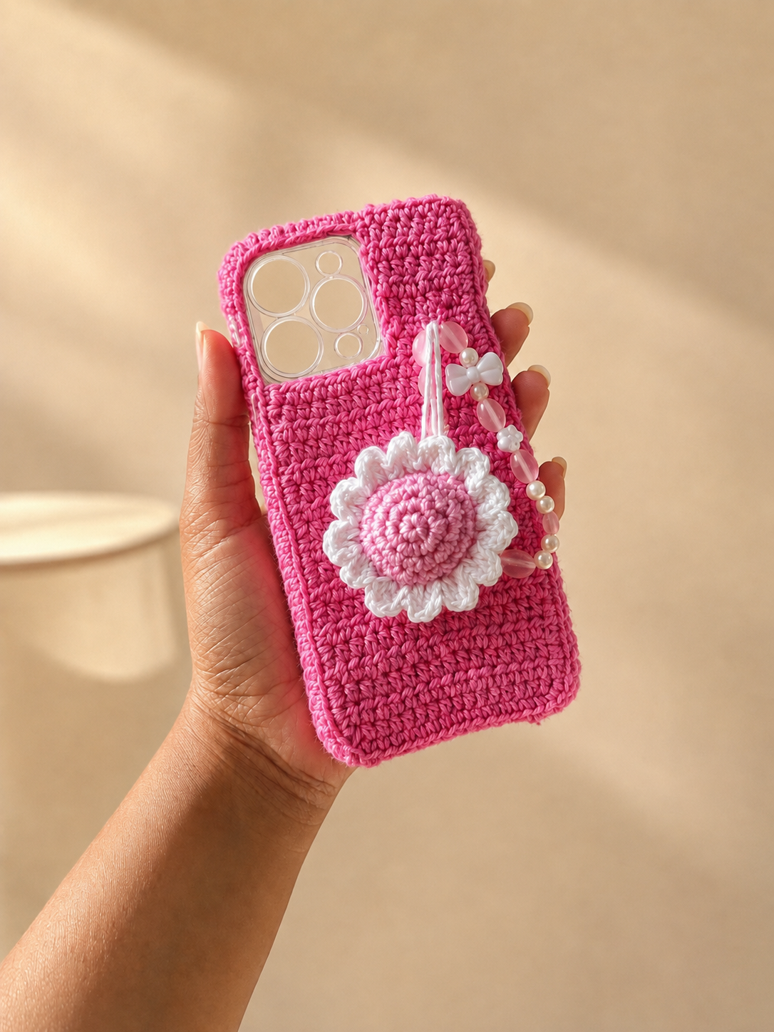 Handmade bright pink crochet phone cover with white daisy charm and beaded bow strap