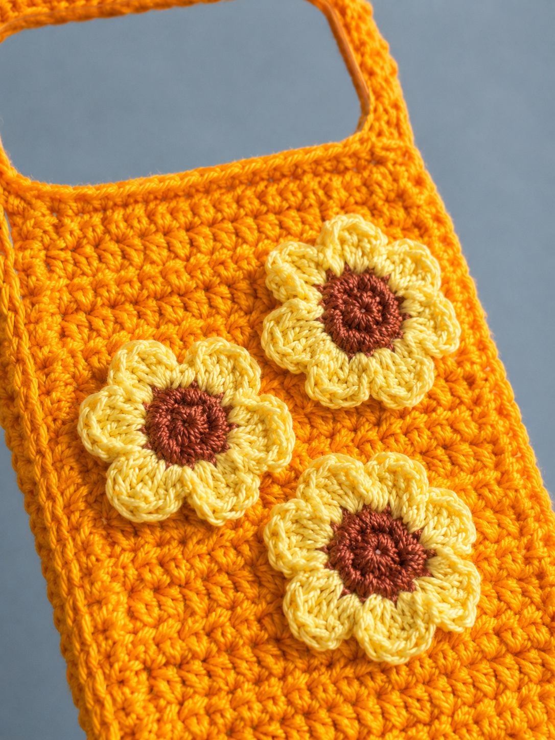 Close-up of three sunflower crochet flowers on an orange phone cover