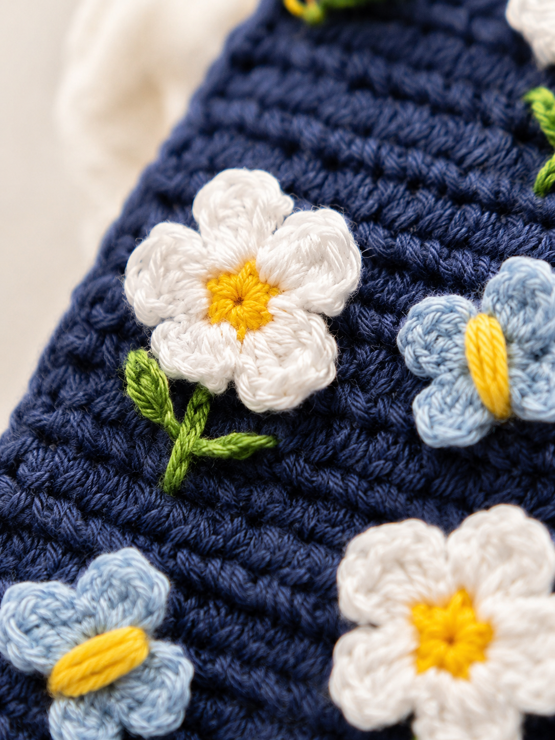 Close-up of white crochet flowers and blue butterfly details on a navy phone cover
