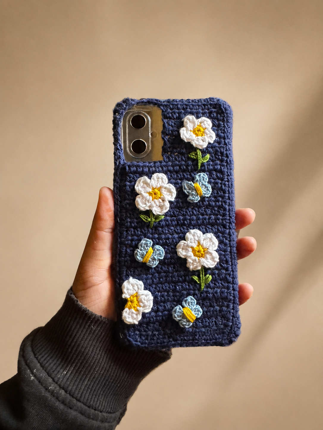 Handmade navy crochet phone cover decorated with white flowers and blue butterflies