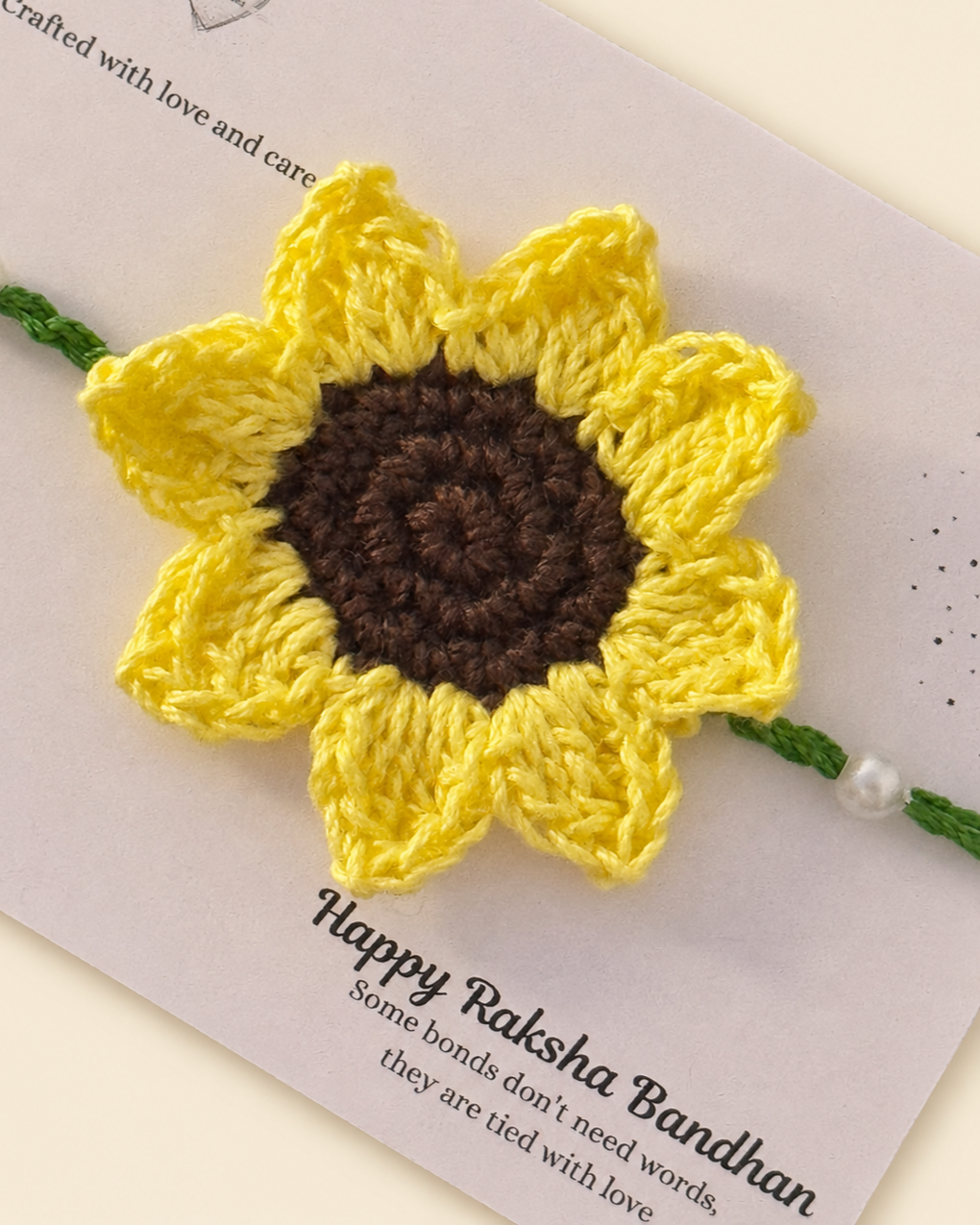 Close-up of handmade sunflower crochet rakhi with green ties and pearl accents