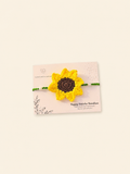 Handmade yellow sunflower crochet rakhi with green ties and pearl accents on a Raksha Bandhan card