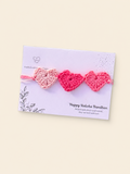 Handmade crochet rakhi with three pink hearts on a Raksha Bandhan presentation card