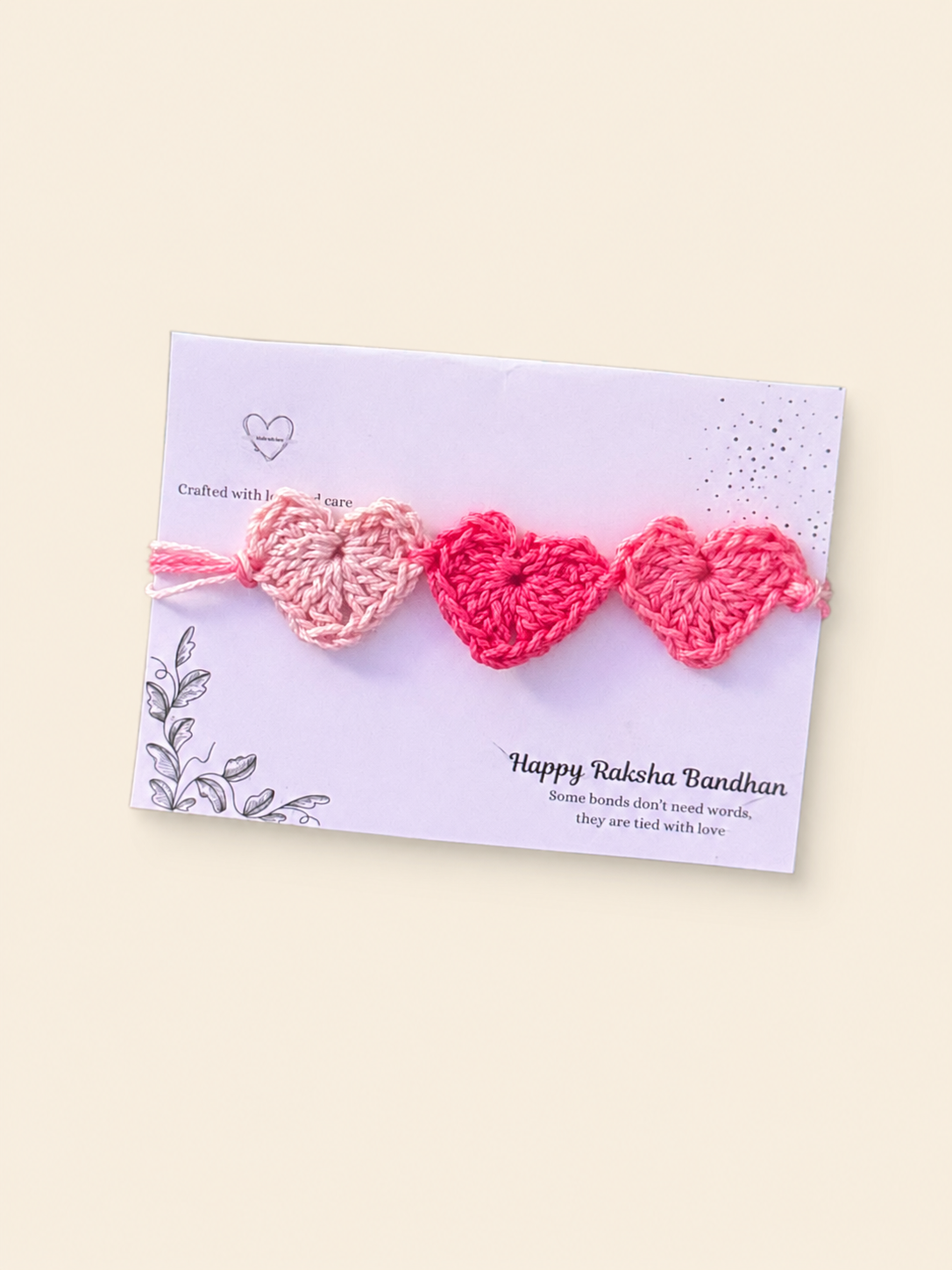 Handmade crochet rakhi with three pink hearts on a Raksha Bandhan presentation card